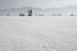 Parents pulling daughter in toboggan on snow, side view