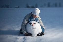 Junge umarmt den Kopf eines Schneemannes, kniend