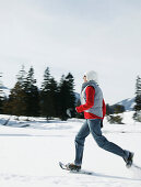 Young woman running with snowshoes in winter landscape