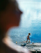 Girl playing with toy sailing boat by lake