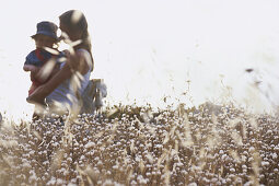 Mother carrying toddler girl in field