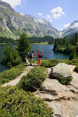 Two hiking women taking a rest in front of a mountain lake Laegh Cavloc, Cavloc Lake, Forno, Bergell, Graubuenden, Grisons, Switzerland