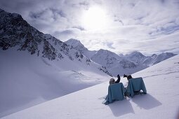 Two young people relaxing on lounge chairs on snow, Kuehtai, Tyrol, Austria