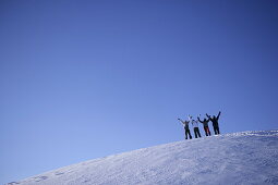 Vier Personen stehen auf schneebedecktem Berghang, Hände in die Höhe, Kühtai, Tirol, Österreich