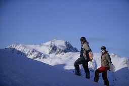 Two persons walking up a snowcapped mountain while carrying a snowboard, Kuehtai, Tyrol, Austria