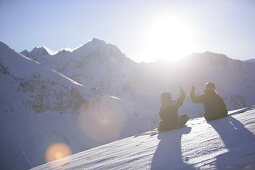 Junge Frau und Mann sitzen im Schnee, klatschen sich ab, Kühtai, Tirol, Österreich