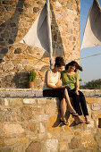 Two women sitting in front of a windmill and reading a book, Antimachia, Kos, Greece