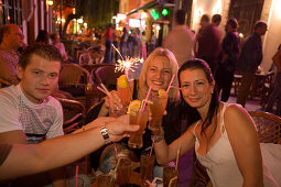 Young people toasting with drinks in an open-air bar at night , Kos-Town, Kos, Greece