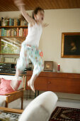 Girl jumping in midair in front of chair