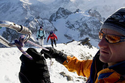 A man, a guide, secures a woman and a man with rope and carabiner on a snowy mountain. Titlis summit, Central Switzerland, Alps, Europe, MR.