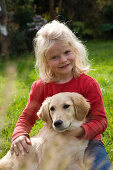 Blond 6 year-old girl holding Golden Retriever on meadow, Germany