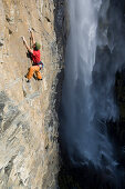 Woman climbing up rock face in front of waterfall, Carinthia, Austria