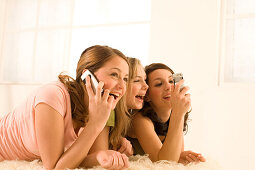 Teenage girls (14-16) on bed using mobil phones