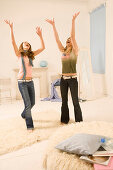 Zwei weibliche Teenager (14-16) springen im Zimmer herum, Arme nach oben