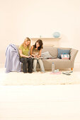 Teenage girls (14-16) sitting on sofa, looking into book