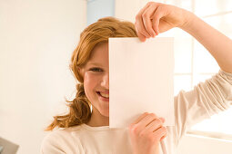 Weiblicher Teenager (14-16) bedeckt Gesichtshälfte mit Briefbogen