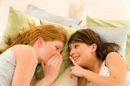 Zwei weibliche Teenager (14-16) liegen auf dem Bett und tuscheln