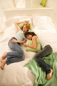 Two teenage girls (14-16) snuggling together on bed, listening to portable MP3 player