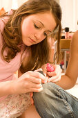 Weiblicher Teenager (14-16) lakieren sich die Fingernägel, Weibliche Teenager (14-16) lakieren sich die Fingernägel