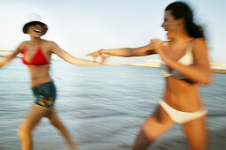 Two young women running on the beach, laughing, blurred motion
