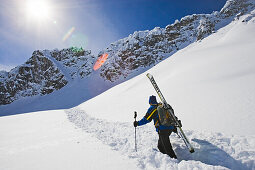 Auf der Suche nach unverspurtem Pulverschnee. Ein Mann wandert mit seinen Skiern auf dem Rucksack durch einen Schneehang. Lech, Zürs, Arlberg, Österreich, Alpen, Europa.