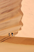 Eine junge Frau und ein junger Mann besteigen Big Daddy, eine der höchsten Dünen der Welt. Die Sossusvlei Dünen. Namib Wüste. Namibia. Afrika. MR