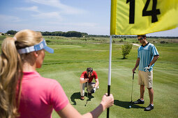 Male golfer preparing to hit ball, young woman giving pointers, Apulia, Italy