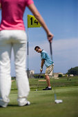 Male golfer preparing to hit ball, woman standing in front, Apulia, Italy
