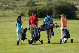 Group of people walking on golf course pulling golf bag on wheels, backview, Apulia, Italy