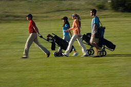 Group of people walking on golf course pulling golf bag on wheels, sideview, Apulia, Italy