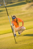 Female golfer lining up ball on putting green, Apulia, Italy