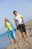 Couple walking with poles on beach, Apulia, Italy