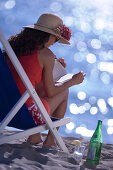 Young woman in deck chair reading a book, Apulia, Italy