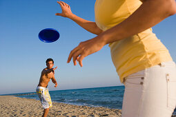 Junges Paar spielt Frisbee am Strand, Apulien, Italien
