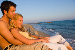 Young couple sitting on beach, sea shore, Apulia, Italy