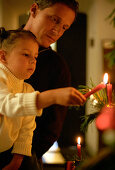 Girl (3-4 years) light up a candle on christmas tree