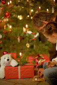 Father and daughter sitting under christmas tree, eating cookies