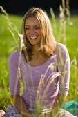 Young woman sitting on meadow, Blades of grass in foreground