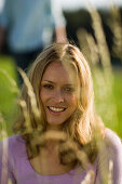 Young woman sitting on meadow, unrecognizable person in background