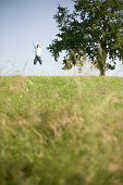 Young man jumping high on meadow, arm raised