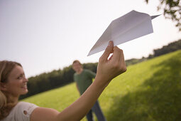 Junge Frau mit Papierflugzeug, auf einer Wiese
