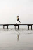Junge Frau joggt auf einem Steg am See