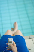 Woman sitting on edge of swimming pool, listening to MP3 player