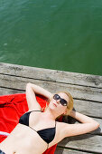 Young woman sunbathing on jetty, wearing black bikini top, Starnberger See, Upper Bavaria, Germany
