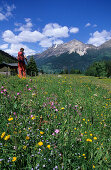 Hiker in a field of flowers and view to Sassalb mountain range, Puschlav, Grisons, Switzerland