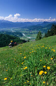 Aussichtsbank mit Wanderer in eine Blumenwiese am Kranzhorn, Blick auf Inntal und Zentralalpen, am Kranzhorn, Chiemgauer Alpen, Tirol, Österreich