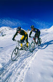 Two mountain bikers riding through deep snow, Serfaus, Tyrol, Austria
