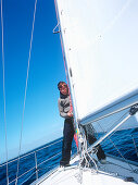 sailor working on sailing boat, german; baltic sea, germany, denmark; sailing; set the sails; strike the sails; male; man; transport; moving forward; standing on boat; clear sight; wind; windy; trip; cruise; vacation; holiday; travel; journey; adventure; 