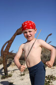 Boy playing pirate between rosty anchors on beach, Ilha de Tavira, Tavira, Algarve, Portugal
