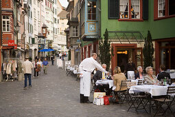 Waiter serving a drink in a pavement cafe, view inside Augustinergasse with ornated bay windows, Zurich, Canton Zurich, Switzerland